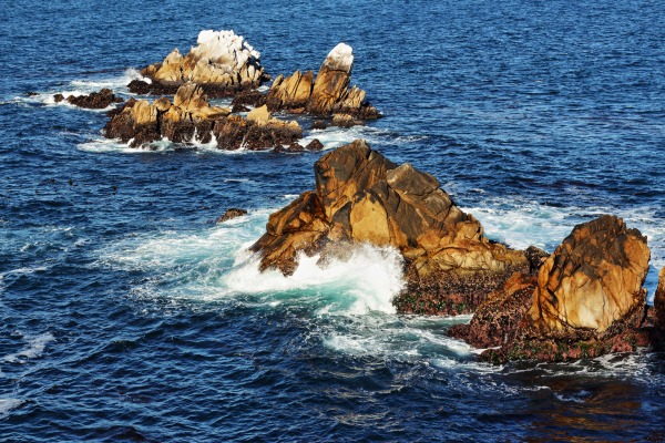 Clear blue ocean waves breaking on rocks in daylight